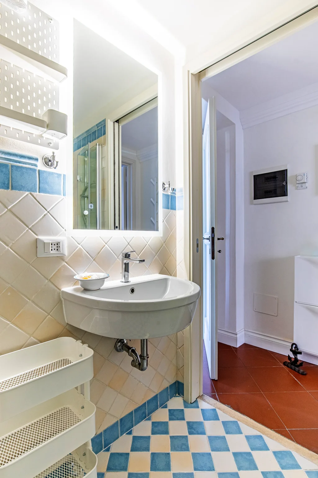 Il bagno della Camera Blu, con lavabo, specchio illuminato e pavimento a scacchi azzurri