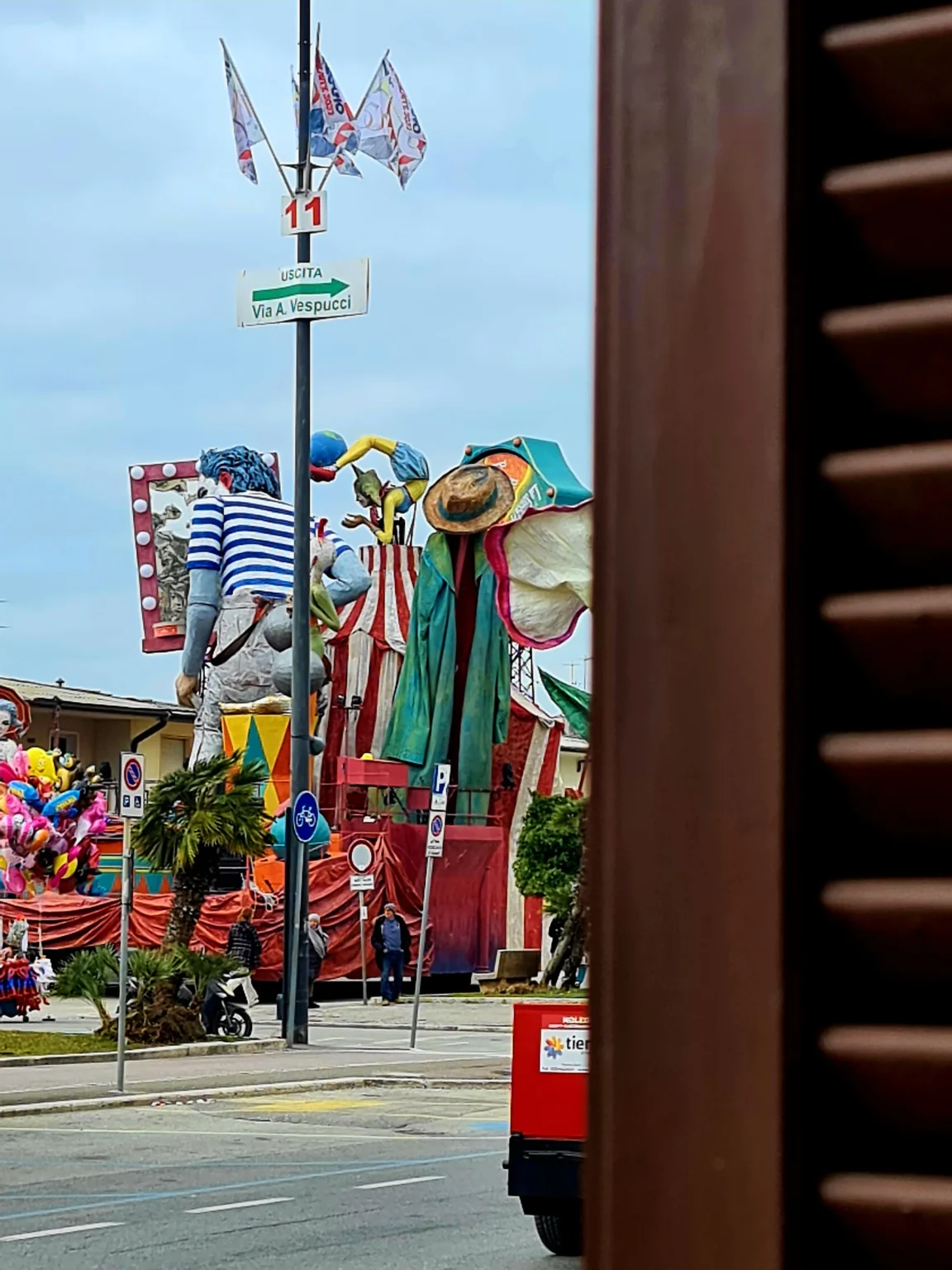 Un char du Carnaval de Viareggio à l'arrêt dans la rue avant le défilé, vu de la porte-fenêtre de Suite Carducci Viareggio, volet ouvert