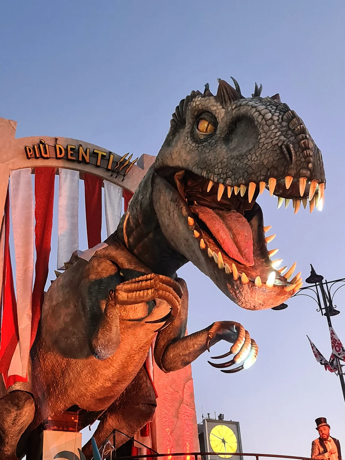 Un dinosaure en papier mâché à la gueule grande ouverte, sur un char du Carnaval de Viareggio au coucher du soleil
