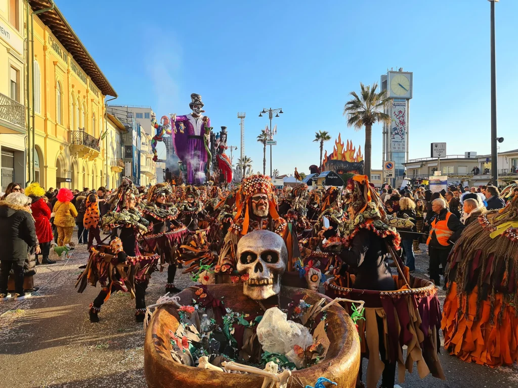 Une mascarade en costumes aux tons terre et orange défile sur le front de mer de Viareggio, entre le public, les immeubles et la tour de l'horloge