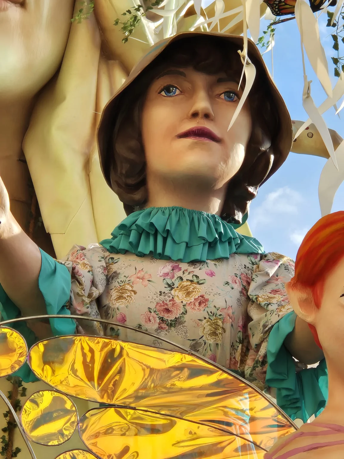 Le visage d'un personnage en papier mâché coiffé d'un chapeau et vêtu d'une robe à fleurs, vu de près