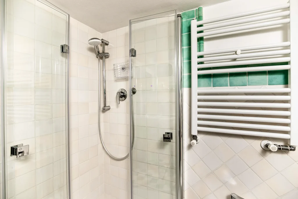 La ducha con mampara de cristal y el radiador toallero del baño de la Habitación Dorada