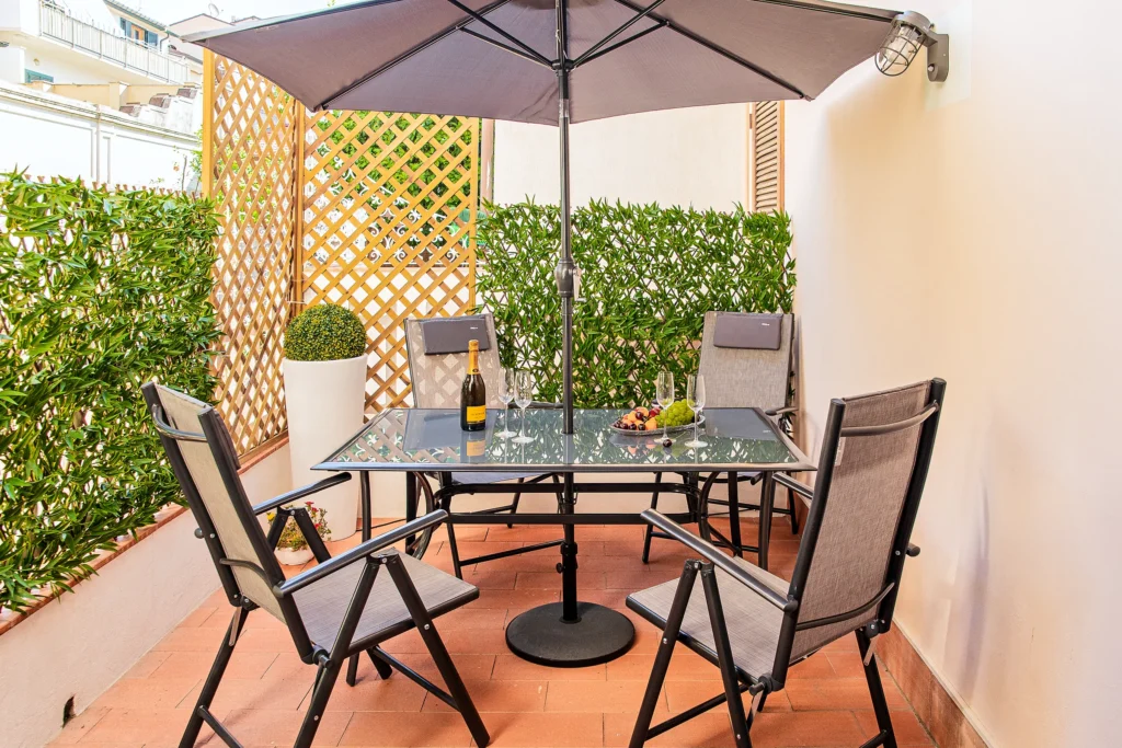 El patio privado de Suite Carducci Viareggio con la mesa, las sillas, la sombrilla y el seto verde