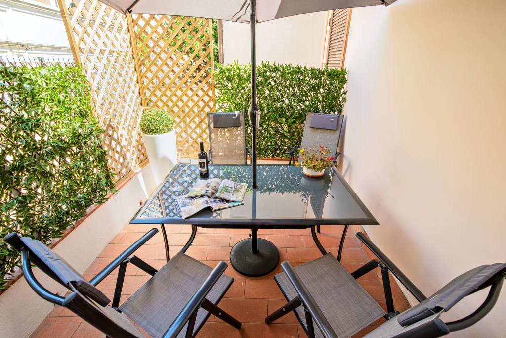 La mesa del patio con una botella de vino y unas revistas, a la sombra, bajo la sombrilla