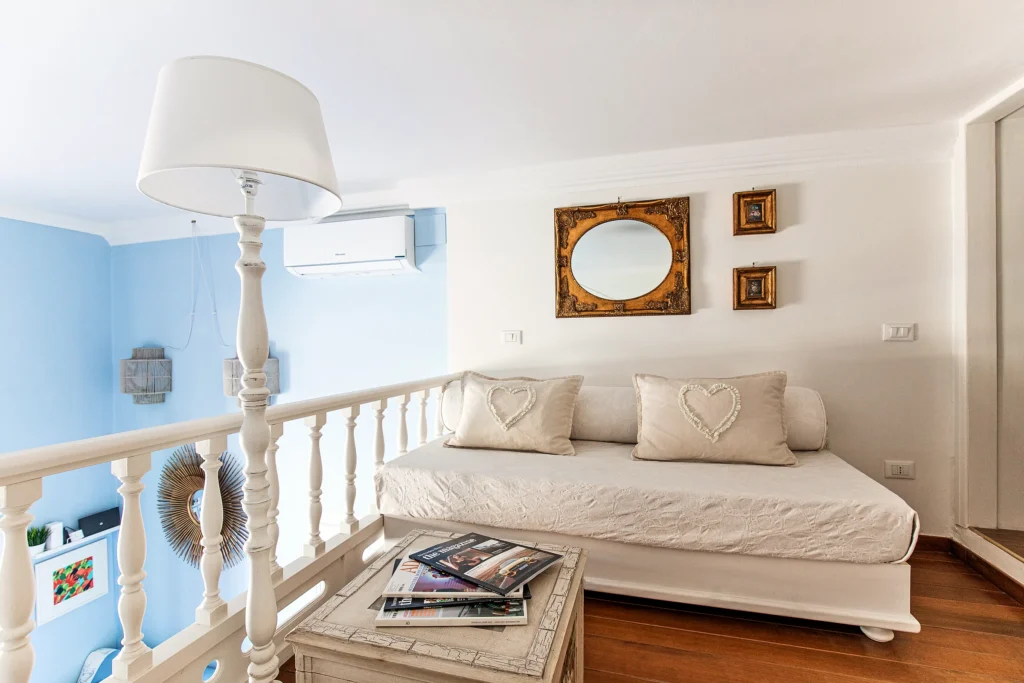 El saloncito del altillo con un sofá cama, la barandilla blanca y el espejo dorado