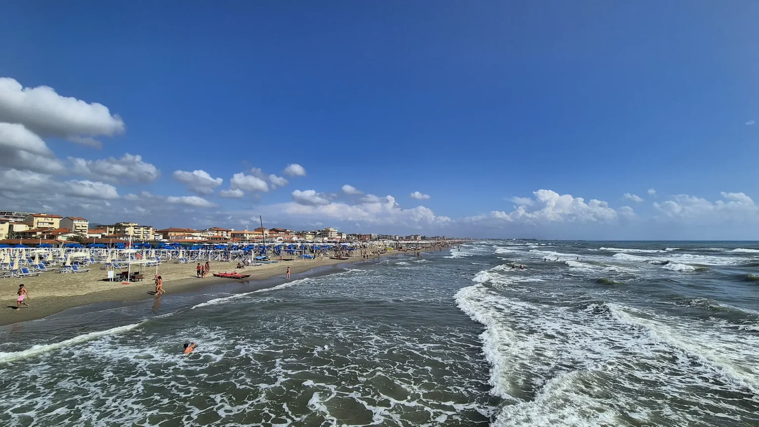 Le onde sulla spiaggia di Viareggio ad agosto, con la città e le Alpi Apuane sullo sfondo