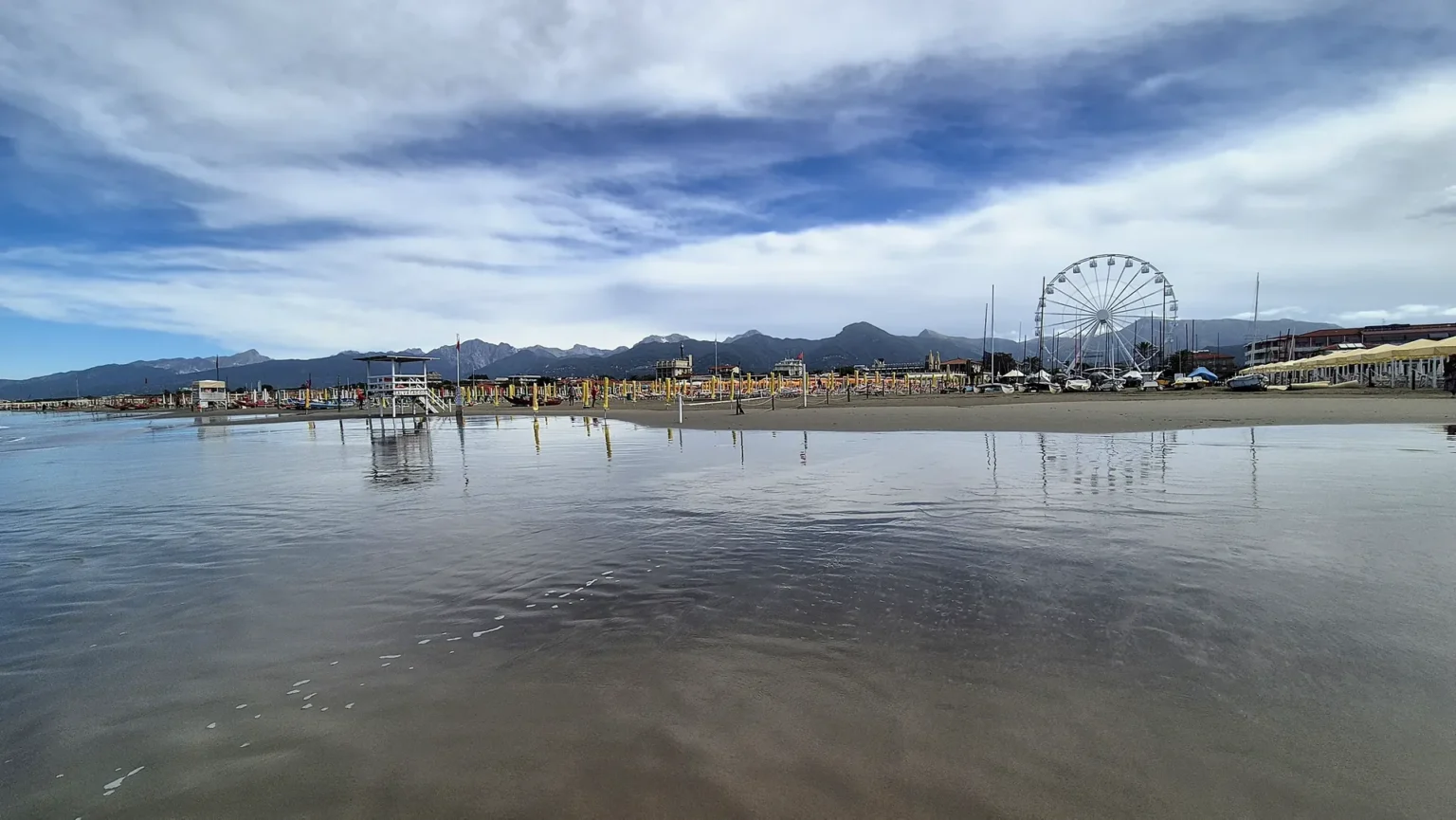 La spiaggia di Viareggio bagnata dal mare, con i riflessi del cielo e la ruota panoramica