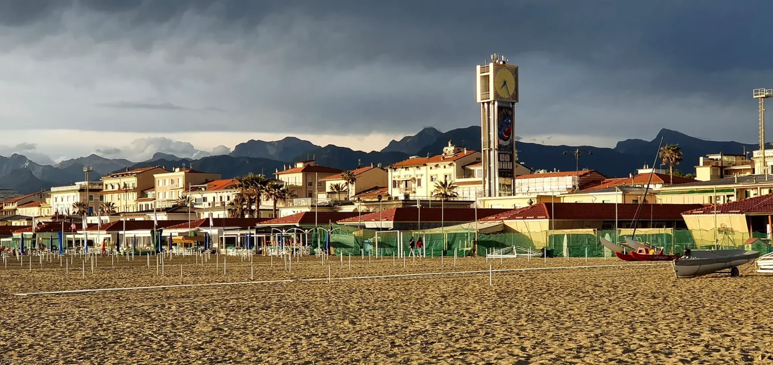 La spiaggia di Viareggio con la torre dell'orologio e le Alpi Apuane, sotto un cielo da temporale